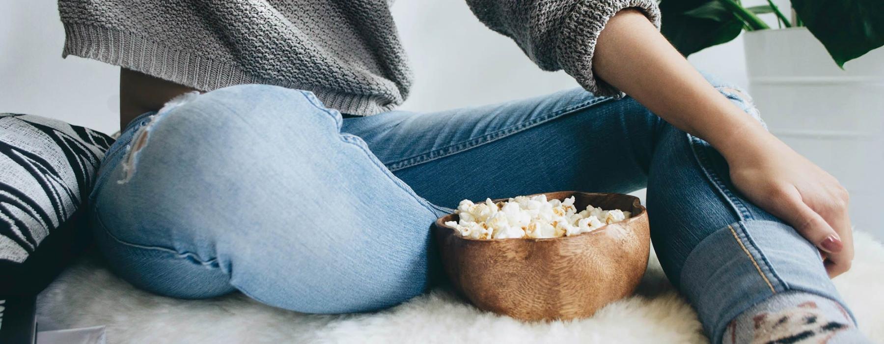 woman sits on a rug with a bowl of popcorn